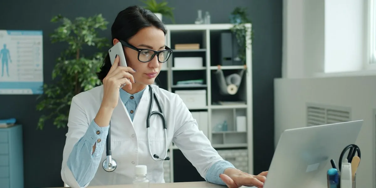 A clinician on the phone while working on a laptop in a medical office